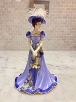 Front view of porcelain lady bell showing lavender dress, umbrella, gold trim, feathered hat