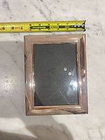 Front view of frame showing inner opening and reflective rose-gold finish with tape measure indicating approx. 5.5" width