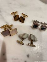 Four pairs of cufflinks laid out, showing front designs and finishes