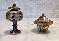 Both cloisonné vessels with lids displayed on countertop