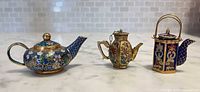 Front view of three miniature cloisonné teapots showing shapes and enamel designs