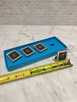 Four small silver picture frames in tray with tape measure for scale