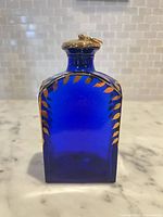 front view of cobalt blue perfume bottle with stopper showing gold enamel leaf border
