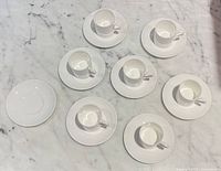 Top view showing seven cups on saucers and extra saucer