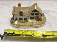Front angled view of resin Anne of Green Gables house figurine with tape for scale