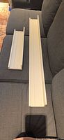 Two white Ikea Mosslanda shelves on sofa showing full lengths