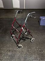 Front left view of metallic burgundy rollator walker showing frame, wheels, hand brakes