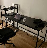 Desk in use showing shelving with electronics and chair nearby