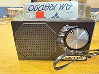 Front view of black Omnitron AM radio with speaker grille, tuning dial, strap visible