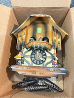 Front view of chalet cuckoo clock in box with pinecone weights visible