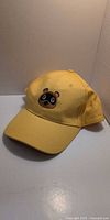 Front view of yellow Animal Crossing snapback cap showing embroidered raccoon face