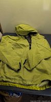 Full view of lime-yellow hooded Nike windbreaker laid flat