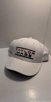 Front view of white TaylorMade snapback cap showing embroidered logo and curved brim