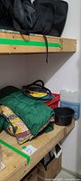 Shelf with green sleeping bag, red crate, pump hose, black speckled pot, blue water container