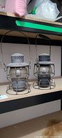 Two grey metal caged globe kerosene lanterns on shelf