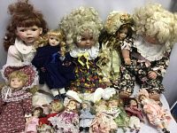 Full group of fifteen porcelain dolls of various sizes, hair colors and outfits, sitting closely packed.