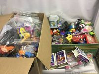 Wide view of boxes containing a variety of kids' toys including character figures and assorted small toys in plastic bags and loose mix.