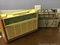 Two vintage radios side by side on a wooden surface, one beige and the other metallic with a handle.