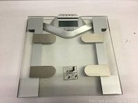 Top view of the square electronic scale with glass platform and metal sensor pads.