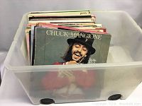 Plastic storage bin containing approximately 50 LP records including a Chuck Mangione album cover facing forward worn and aged.