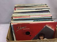 Wide shot of approximately 60 LP records stacked vertically in a cardboard box. Sheena Easton album cover prominently visible.