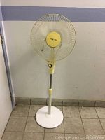Full view of the Airworks pedestal fan showing yellow fan head, white pole, and round base.