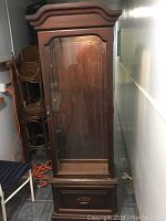 Front view of the tall wood curio cabinet with glass door and drawer at bottom, showing overall structure and finish.