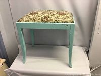 Side view of vintage foot stool showing duck egg blue paint and curved legs with some paint wear.