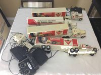 Overview of four white transport trucks with Canadian Tire and Motomaster branding, all with trailers and black wired remote controls, plus one additional cab unit separated from a truck.