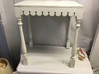 Full view of the folk art table showing white paint, turned legs, scalloped apron edge and square feet.