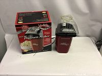 Betty Crocker Hot Air Popcorn Maker in red with black top and clear dome, next to original box on white surface.