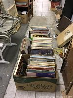 Three large cardboard boxes packed with assorted vinyl LP records. Varied album covers and colors visible on the top layers.