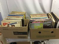 Two large cardboard boxes filled with approximately 150 vinyl LP records showing diverse album covers and mixed condition.