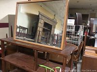 Front view of rectangular mirror propped on wooden furniture reflecting room and fireplace.