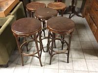 Five wooden bar stools with round seats, three leather/vinyl cushioned and two wooden seats, arranged on tiled floor