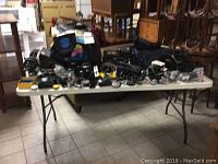 Table showing a large variety of cameras, video recorders, camera bags, and accessories spread over the surface