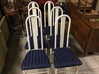 Front view of six metal high back white dining chairs with navy blue striped cushioned seats arranged in two rows.