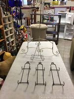 Photo shows five wrought iron pieces on a table: three matching wall plate hangers lying flat and two different sized display easels standing upright with scrollwork design.