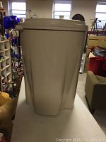 Side view of the beige plastic rain barrel showing its shape and size.