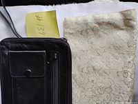 Front view of black leather carry bag beside off-white brocade clutch