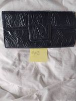 Front view of black embossed clutch showing flap and leaf pattern