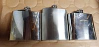 Front view of three stainless steel hip flasks showing polished surfaces