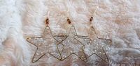 Three gold-tone wire star ornaments laid out on fabric