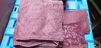 Stack of dark purple hand towels and face cloths displayed on blue tote