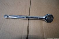 Full view left side of chrome 3/8" drive ratchet wrench on cardboard background