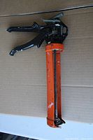Full view of orange caulking gun with black handle