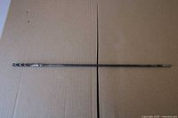 Full view of long steel twist drill bit laid flat on cardboard