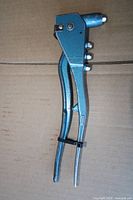 Overall view of teal hand rivet gun showing handles and mounted nosepieces