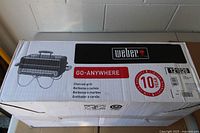Factory-sealed Weber Go-Anywhere charcoal grill box showing product image and warranty label