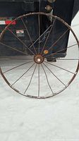 Full view of one rusted wagon wheel leaning against dumpster in snow